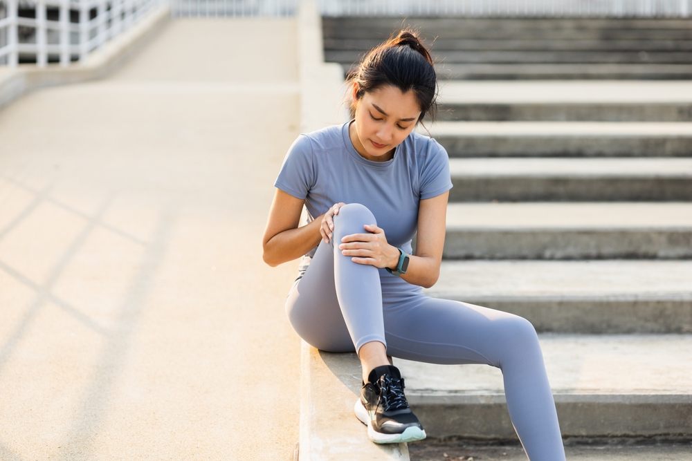 Woman in athletic wear holding knee showing need for orthopedic care consultation