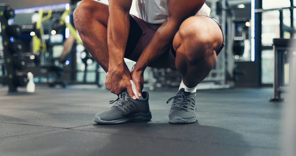 Person holding painful ankle in gym, requiring ankle pain management treatment