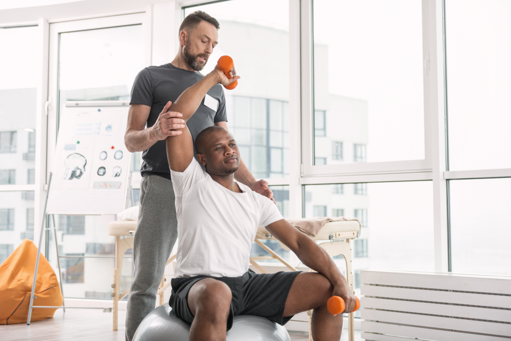 Physical therapist helping patient with arm sling during after surgery care rehabilitation