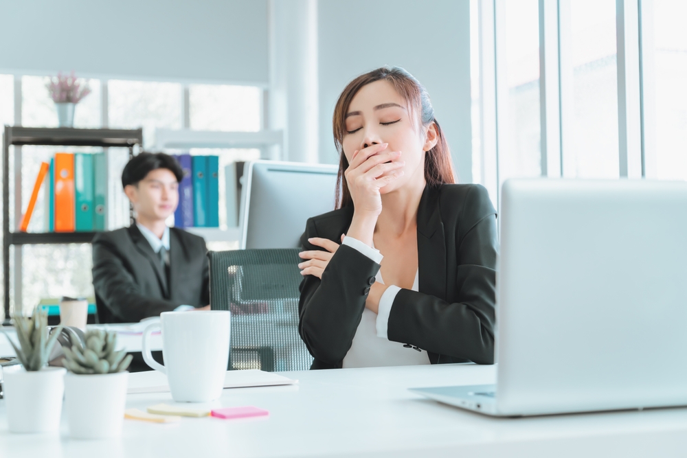 Woman experiencing afternoon fatigue at desk holding head showing tiredness symptoms