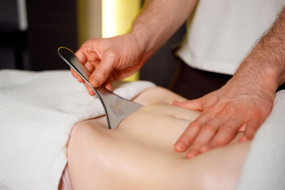Practitioner using stainless steel Graston treatment instrument on patient's leg tissue