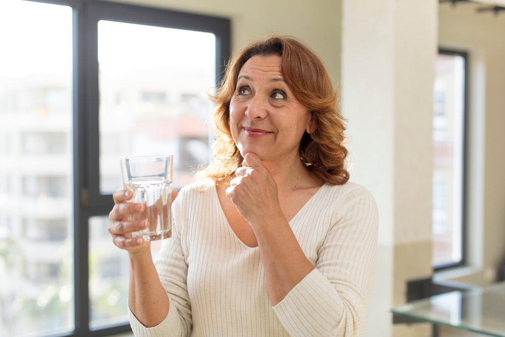 Middle-aged woman taking hormone therapy medication with glass of water