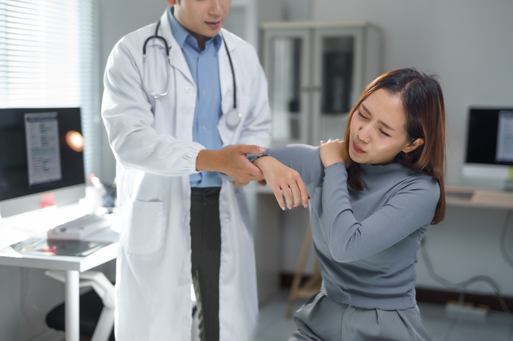 Doctor examining female patient's shoulder during shoulder bursitis treatment consultation