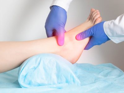 Medical professional examining ankle with highlighted pain area showing tendinitis of the ankle