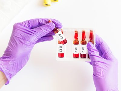 Gloved hands handling vitamin B12 injection vials and ampoules for patient treatment